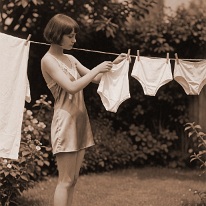 Sweet Promises in the Wind Young woman in a sunny garden hanging a small white swimsuit on a clothesline. She wears a short satin chemise with lace trim and flat sandals. Three other...