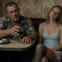 Exhaustion and Isolation at a Corner Table A dockworker with dirt-ingrained hands stares ahead in a dingy nightclub. Beside him, a young woman in a nylon slip leans back with eyes closed, profoundly...
